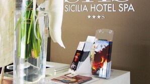 Un mostrador de recepción con un florero, un cartel del Hotel Spa Siciola y algunos folletos.