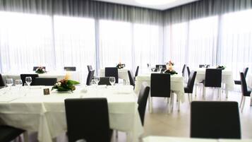 Zona pranzo con tavoli apparecchiati, sedie e un'ampia finestra con tende.