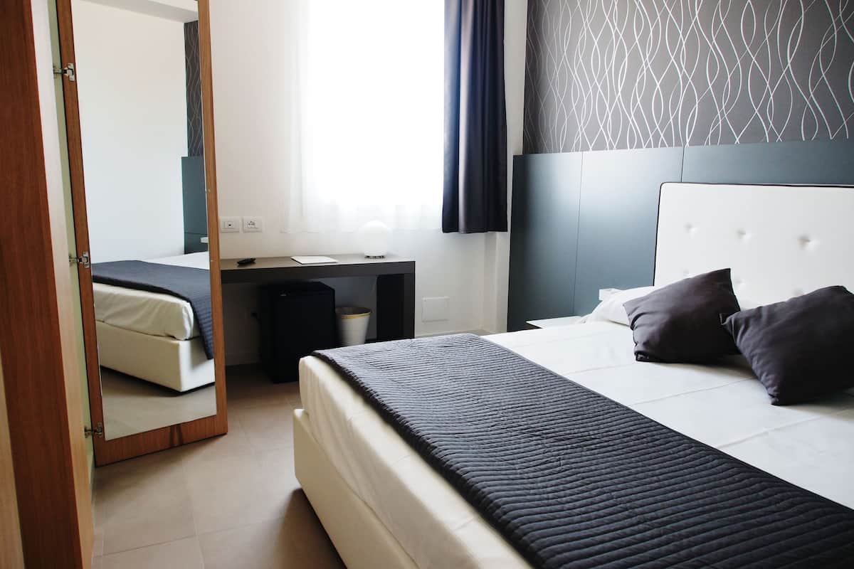 A modern hotel room with a bed, bedside table, and a mirror.