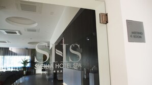 Un moderno vestíbulo de hotel con una recepción, zona de estar y un cartel que indica una sala de reuniones.