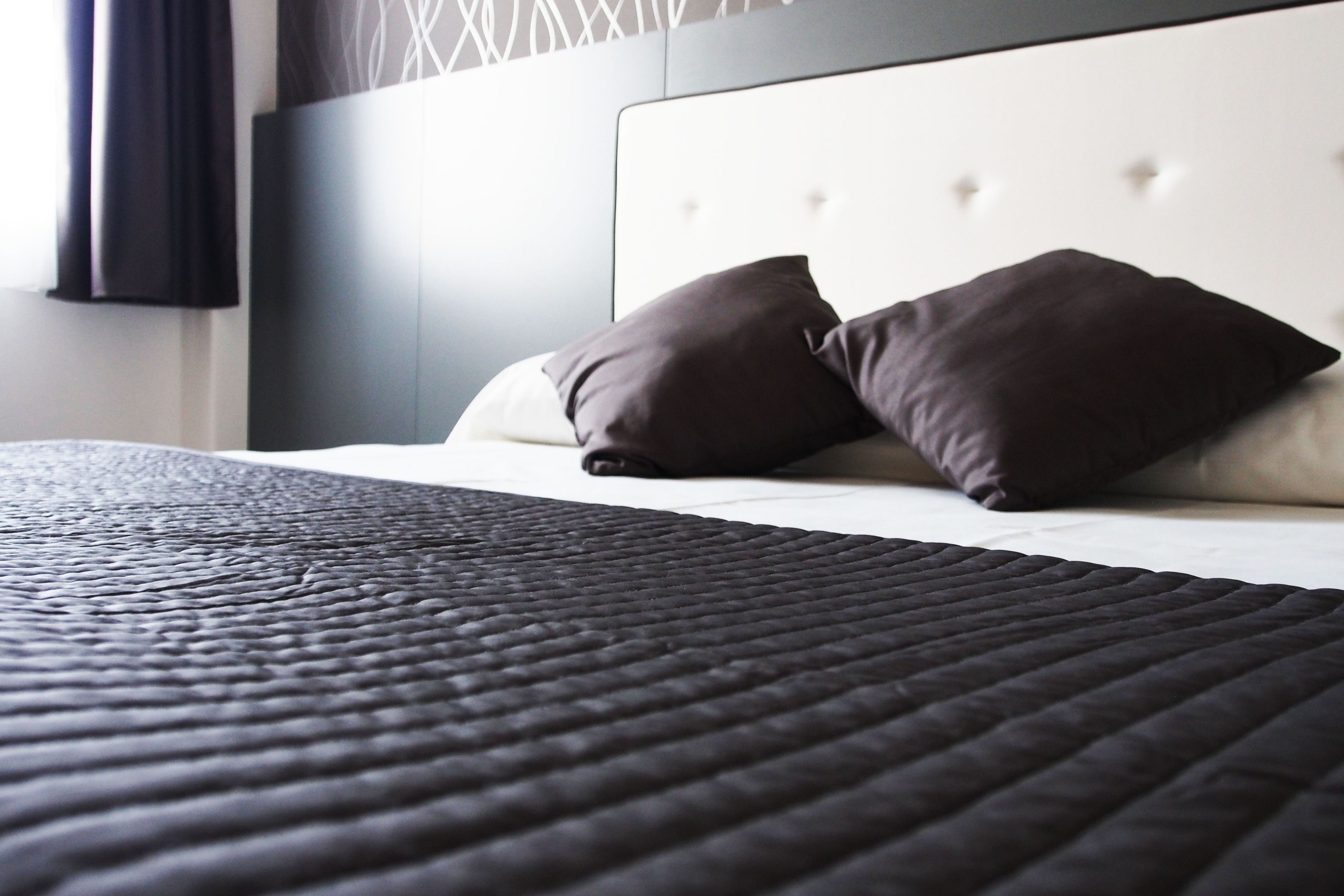 Una cama bien hecha con un edredón oscuro y texturizado y dos almohadas oscuras.
