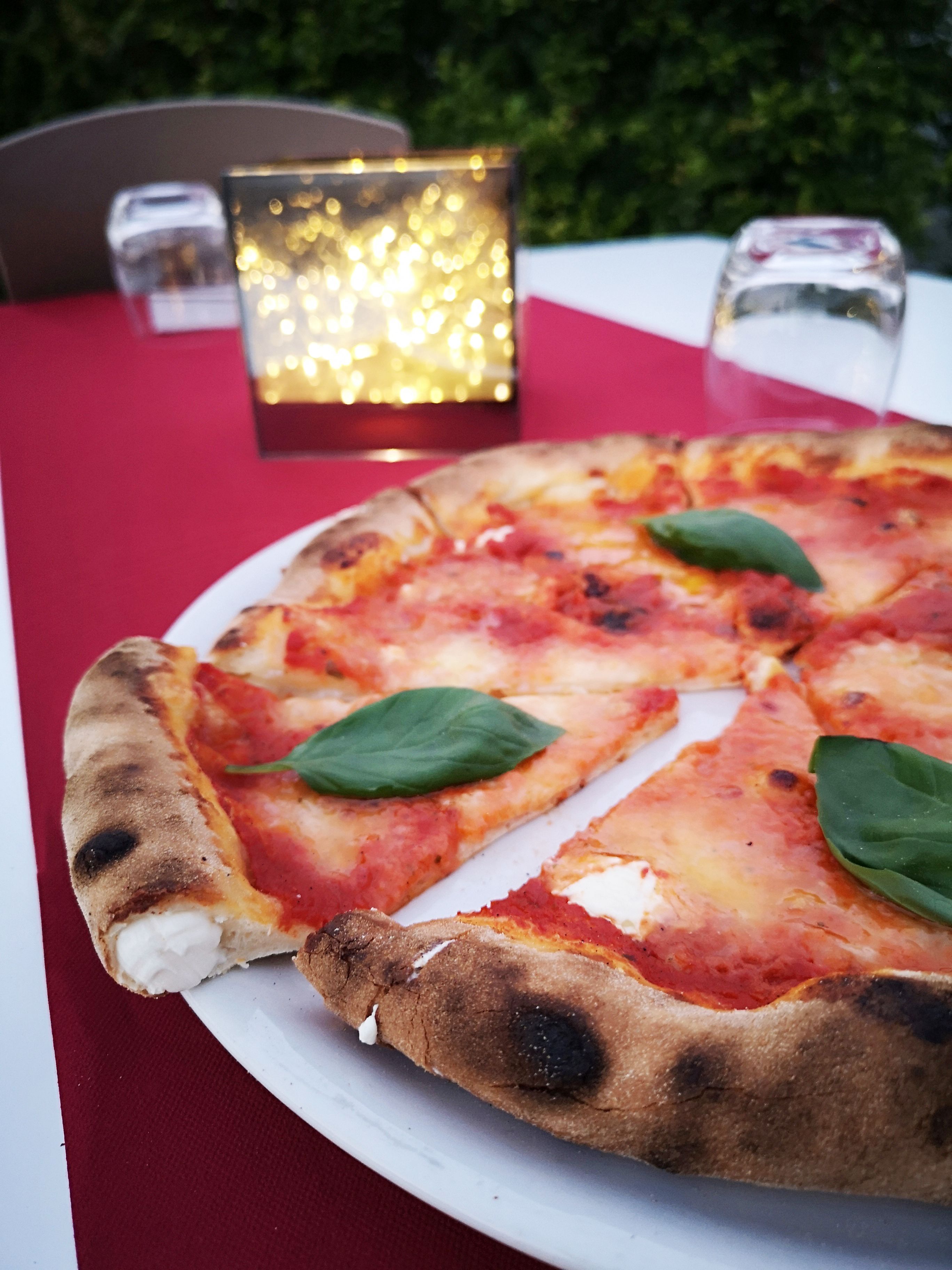 A pizza on a white plate with a red tablecloth, a candle, and salt and pepper shakers on a table.