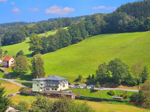 Un hotel con estructura de dos pisos, zona de estacionamiento y vista a una ladera verde.