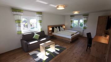 A modern, well-lit room with a sofa, a bed, a small table, and a wooden cabinet.