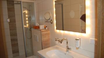 A bathroom with a glass-enclosed shower, a sink with a mirror, and toiletries on the counter.