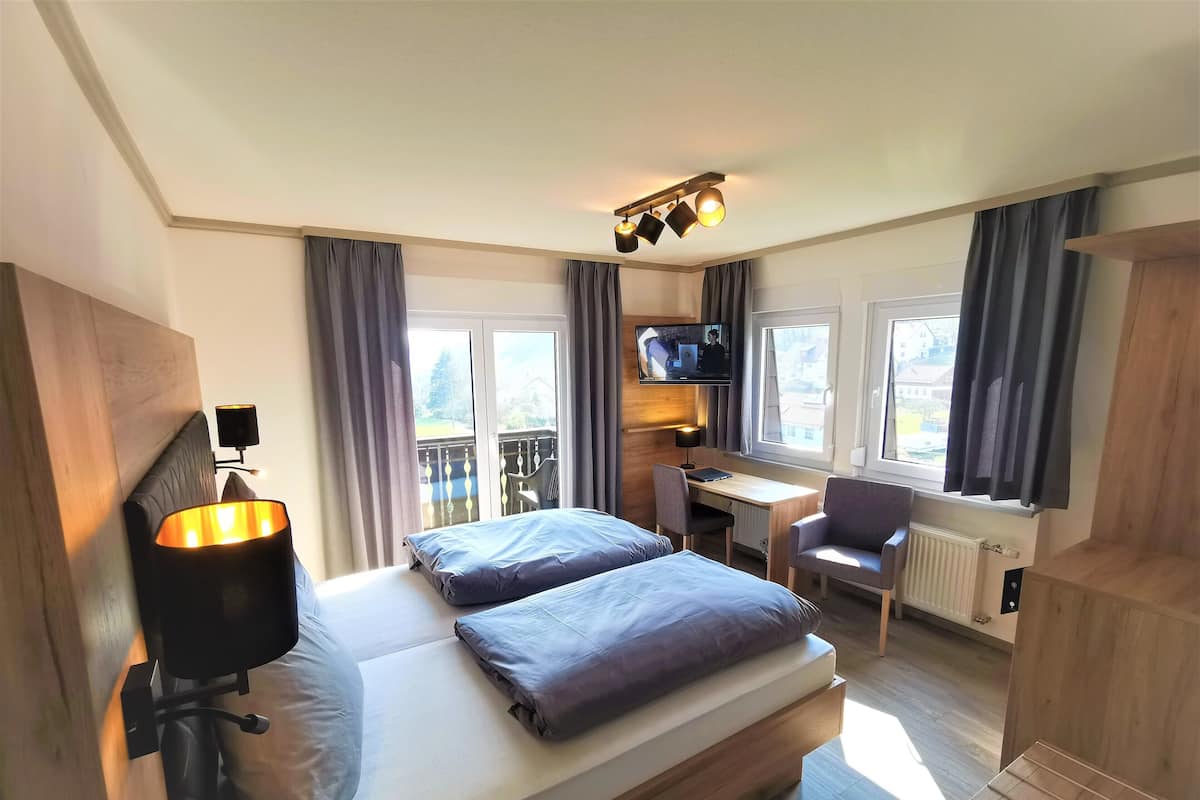 Una camera d'albergo con un letto, una scrivania, una sedia, una televisione e un balcone.