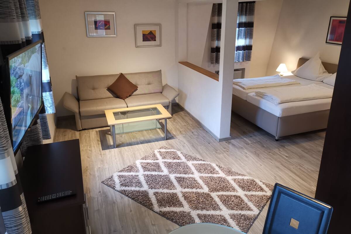Una camera d'albergo moderna con divano, letto, un tavolino e televisore.
