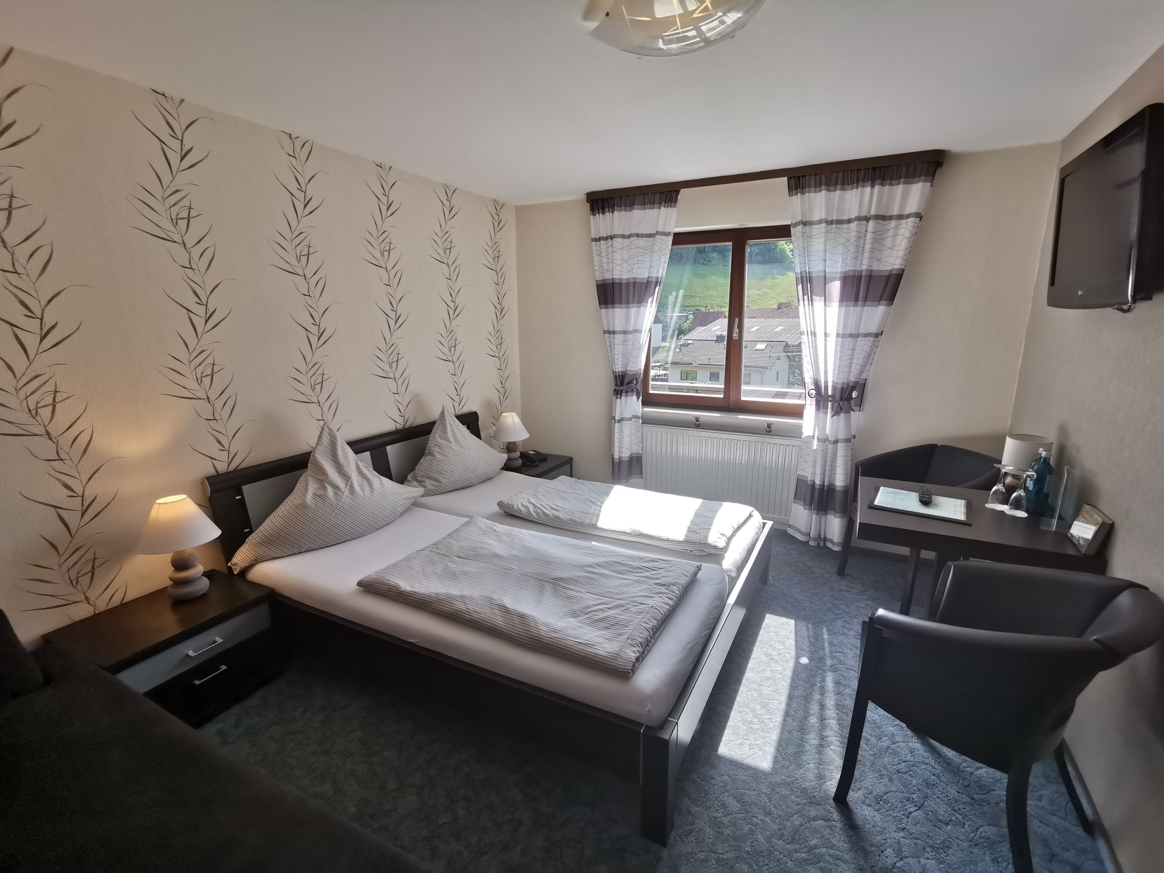 Una habitación de hotel con una cama, mesitas de noche, un escritorio, una silla y una ventana con cortinas.