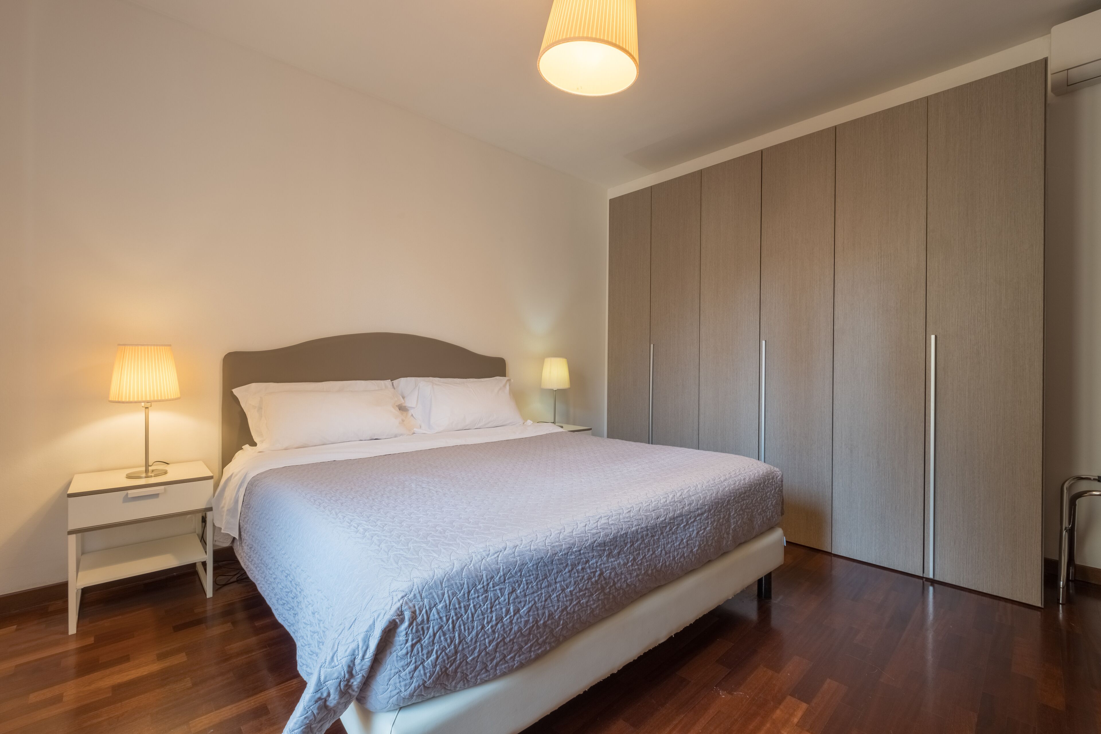 A bedroom with a bed, nightstands, a lamp, and a wardrobe.
