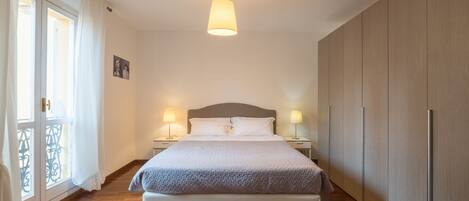 Een slaapkamer met een bed, nachtlampjes, een hanglamp, een kledingkast en een raam met gordijnen.