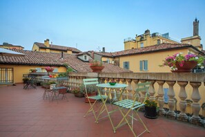 Une terrasse avec une table et des chaises, entourée de plantes en pot et d’une rambarde.