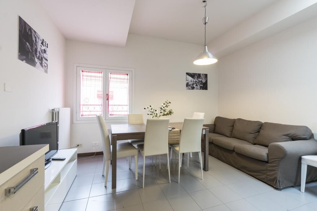 A modern living room with a sofa, dining table, chairs, a TV, and a radiator.