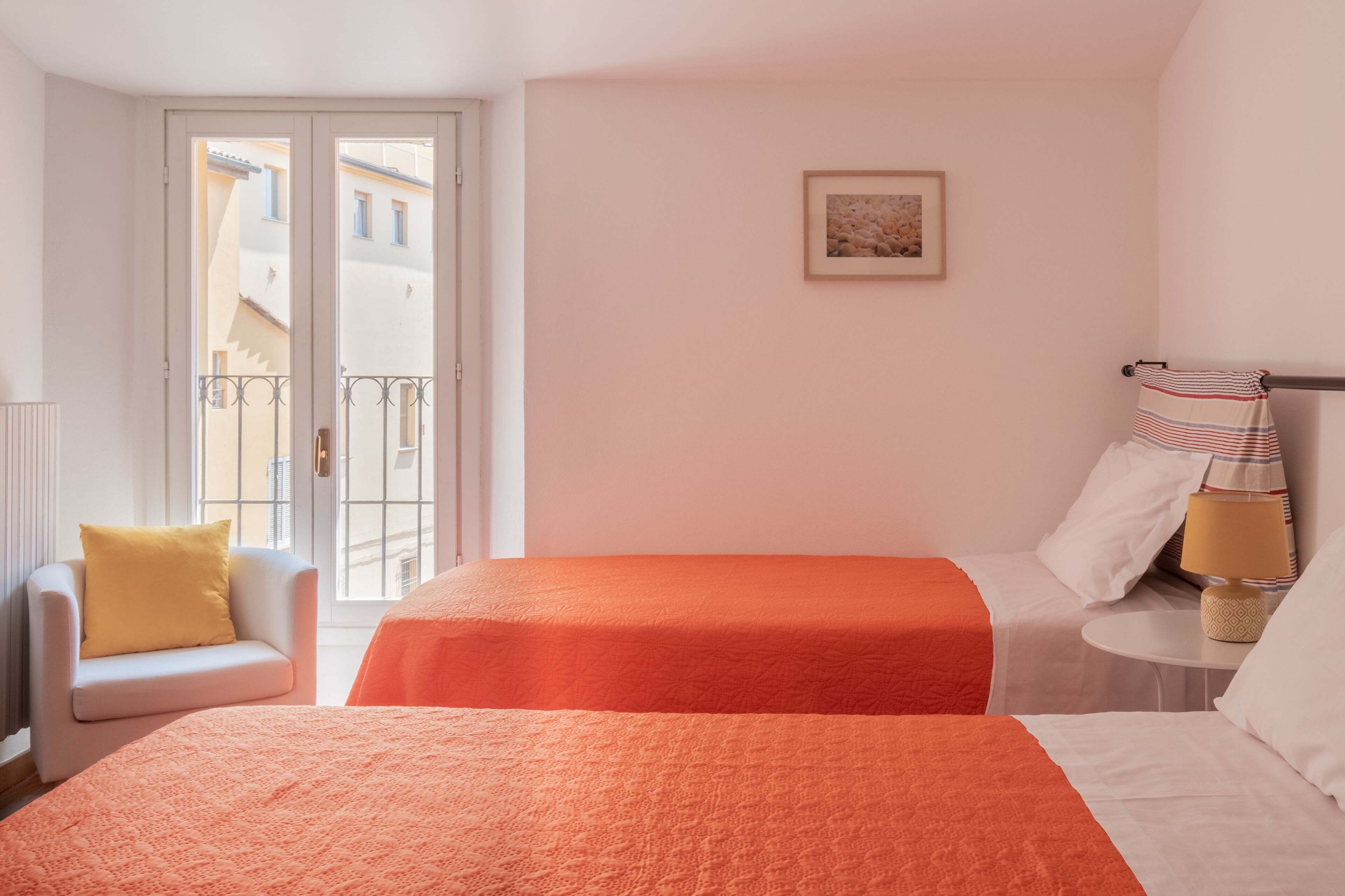 Ein Hotelzimmer mit zwei Betten, einem Balkon, einem Sessel und einem kleinen Tisch mit einer Lampe.