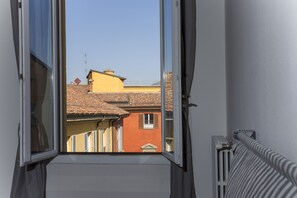 Une vue par la fenêtre sur un bâtiment doté d’un toit recouvert de tuiles et d’une façade jaune.