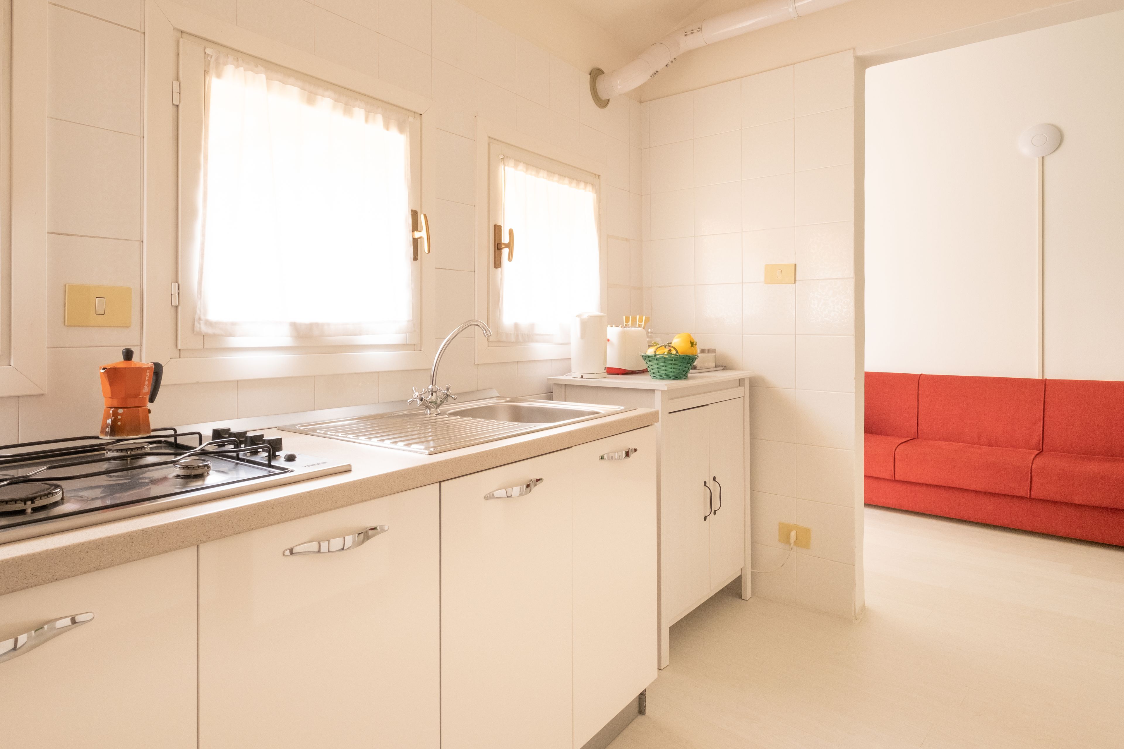 A modern kitchen with white cabinets, a gas stove, and a sink. There is a red couch in the adjacent living area.
