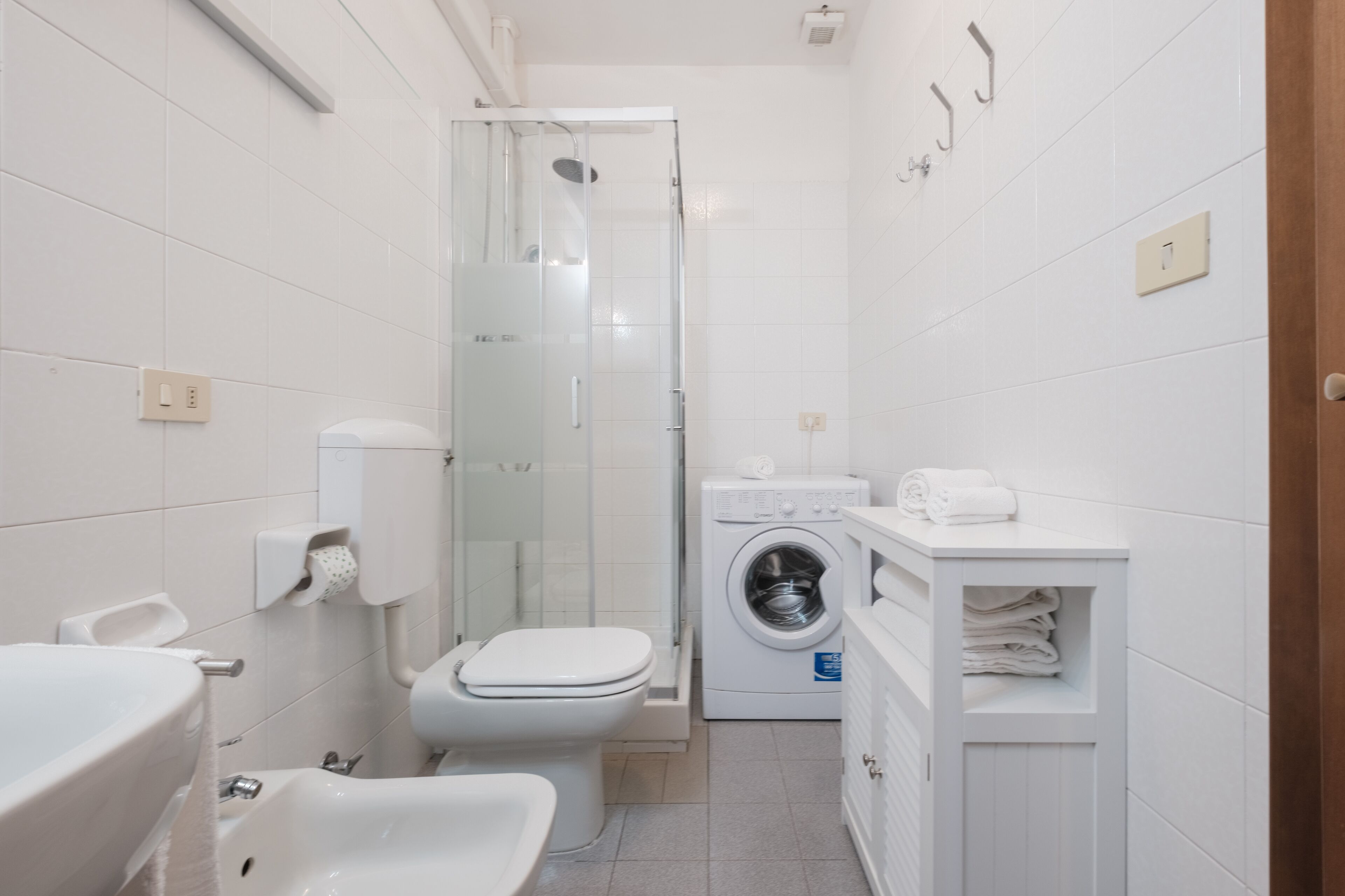 A compact bathroom with a toilet, sink, shower, and washing machine.