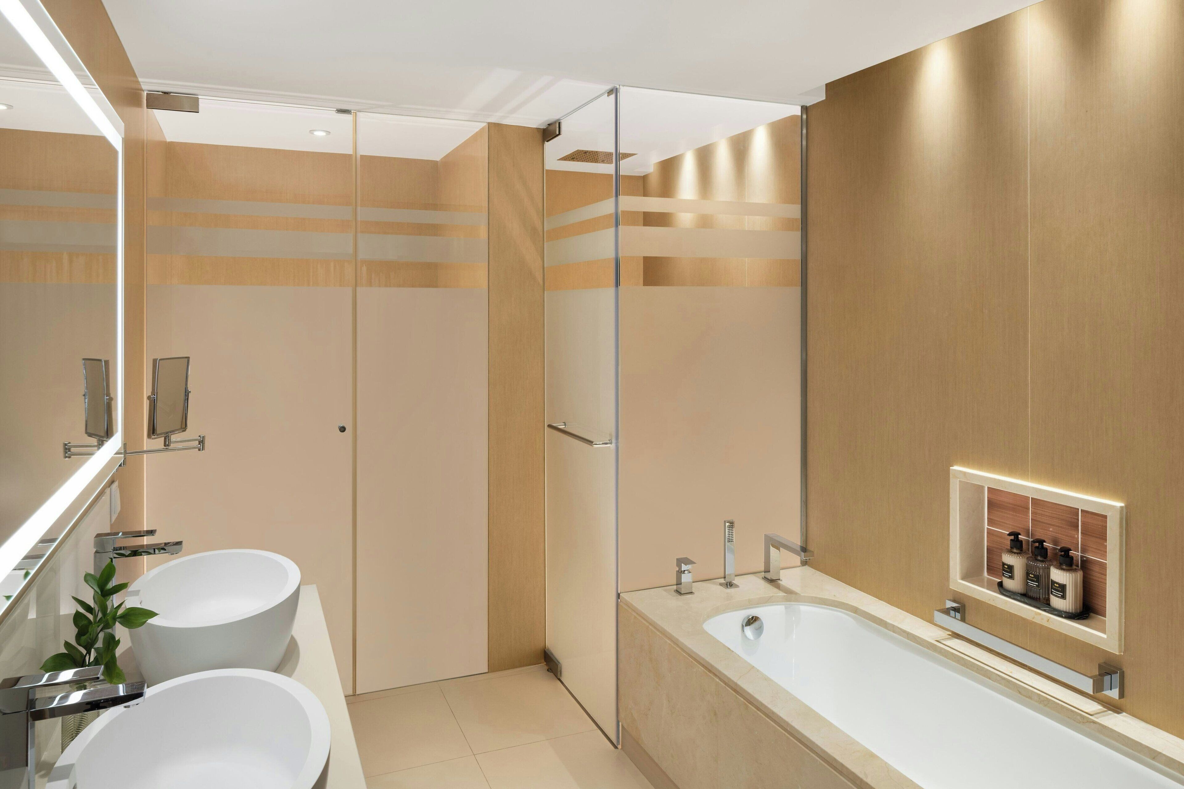 Un baño moderno con dos lavamanos, una bañera grande y un box de ducha de cristal.