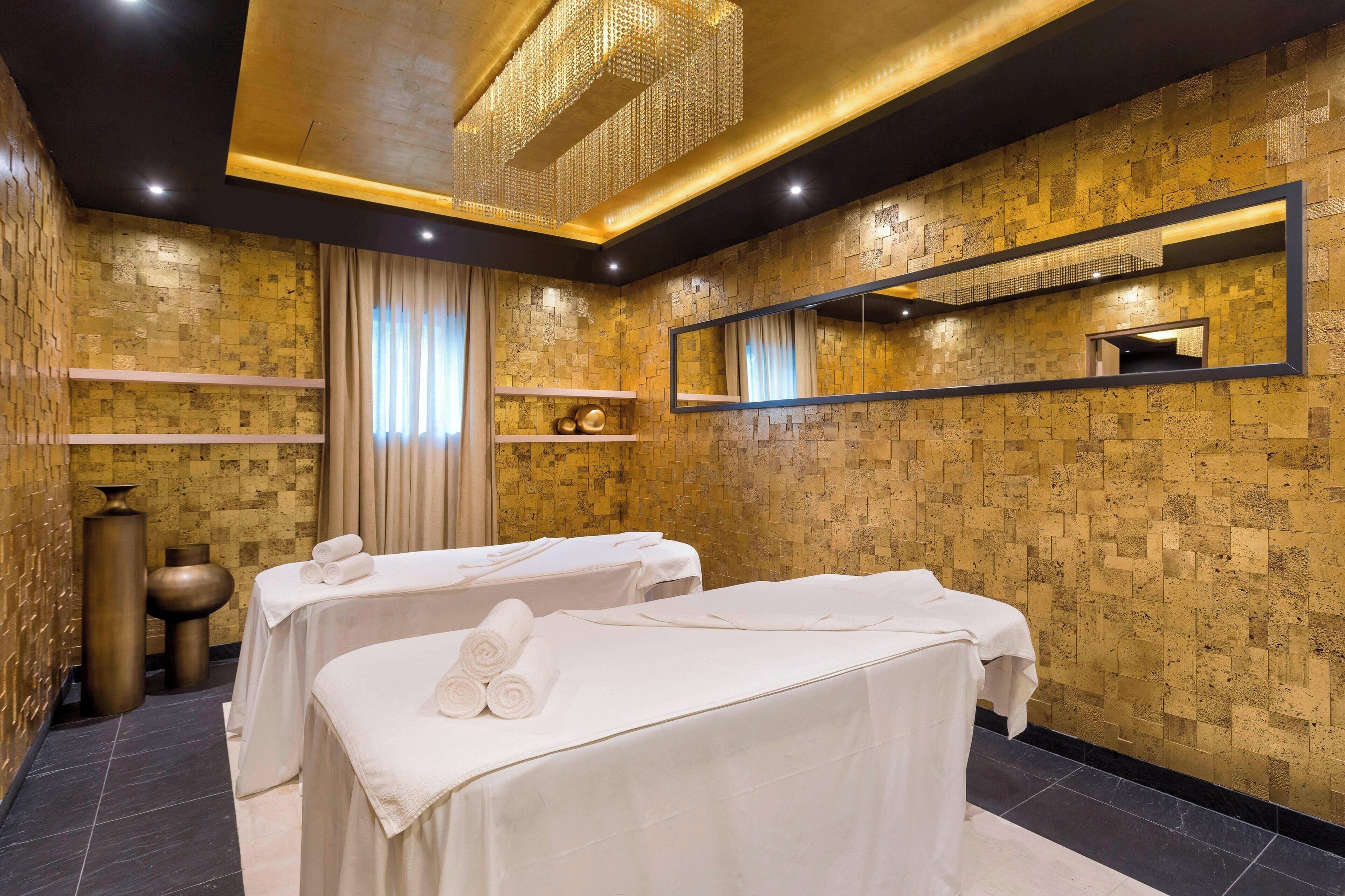 A spa room with two massage tables, a large mirror, and a decorative chandelier.