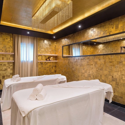 A spa room with two massage tables, a large mirror, and a decorative chandelier.
