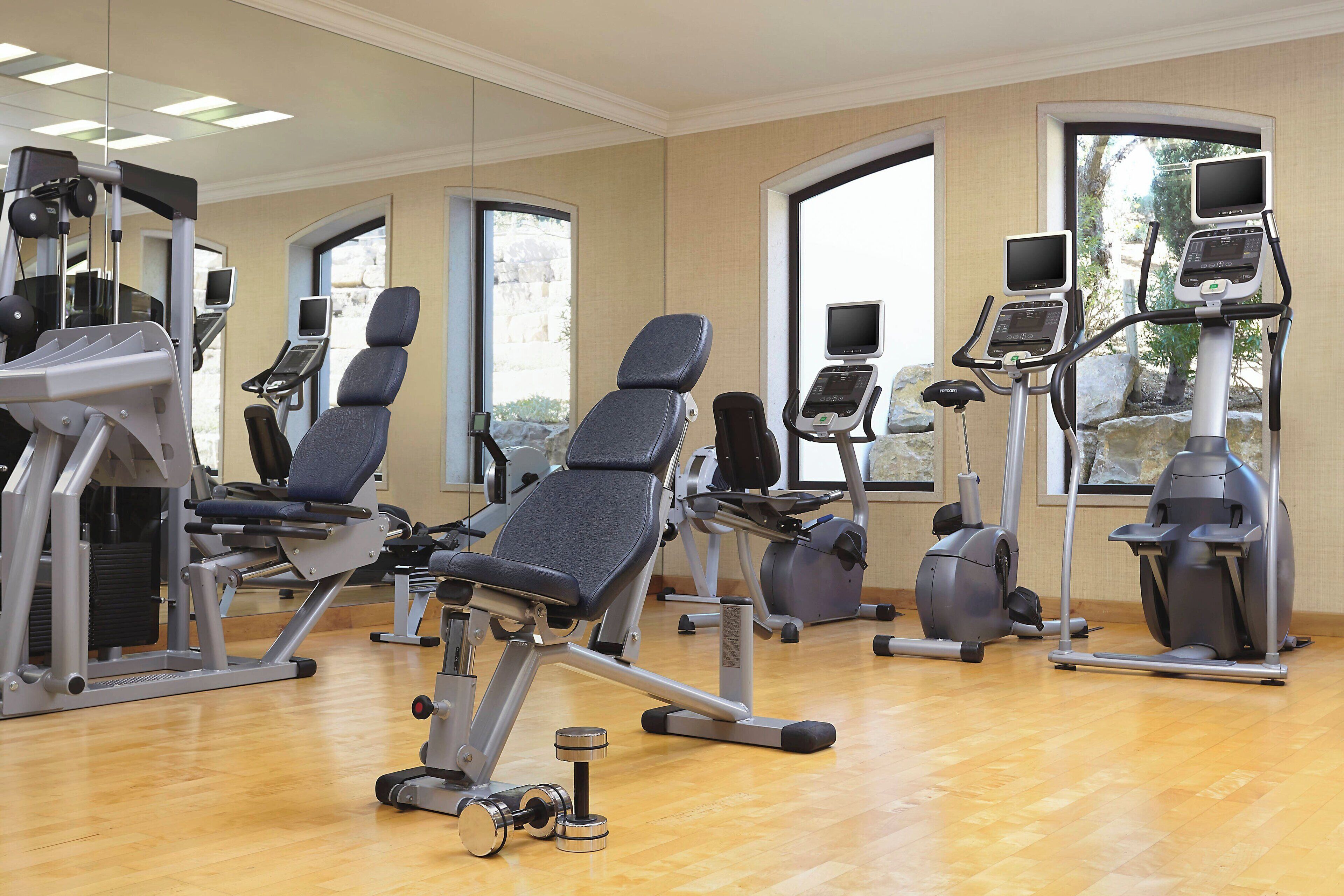 A gym with exercise equipment, large windows, and a wooden floor.