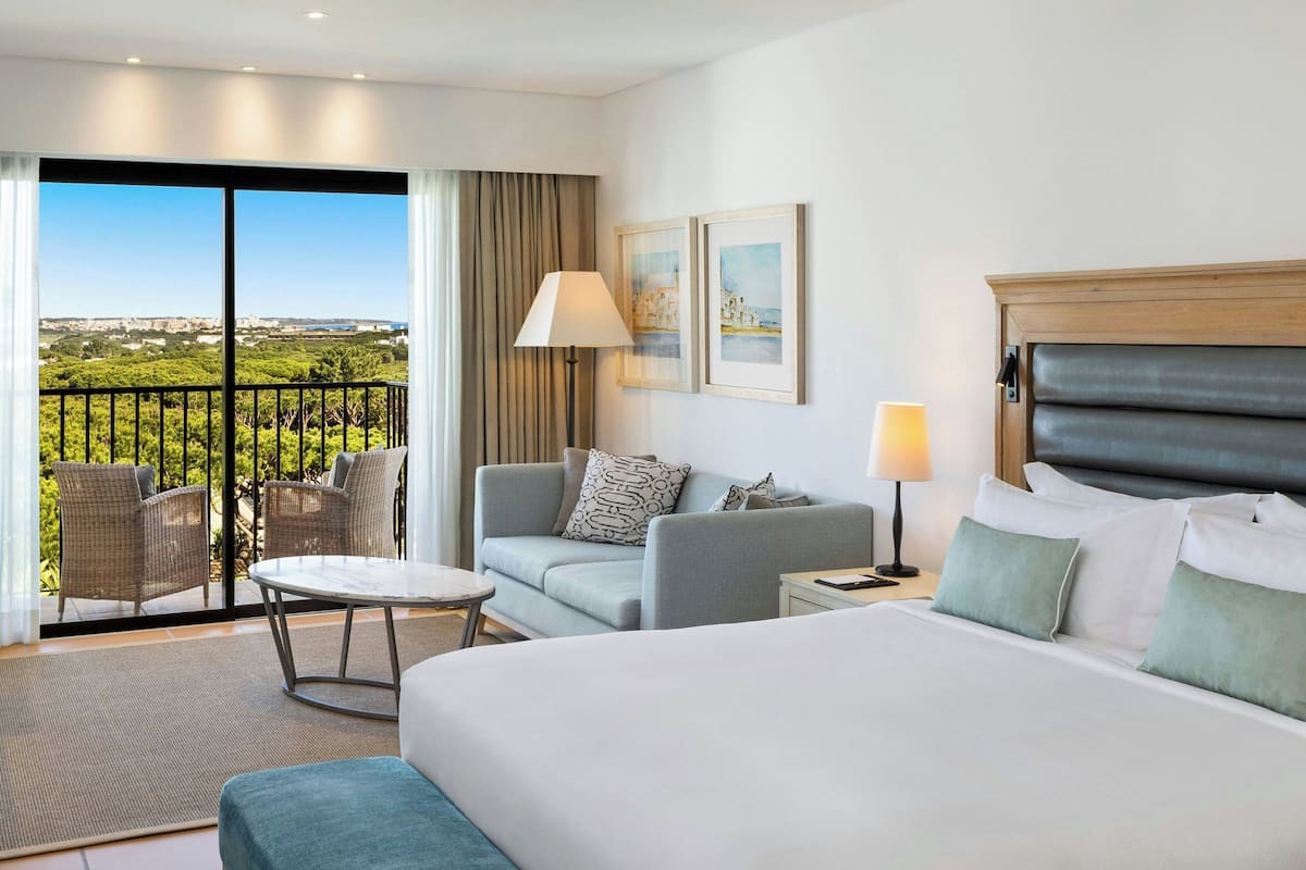 Une chambre d’hôtel avec un balcon, un lit, un canapé, une table et deux lampes.