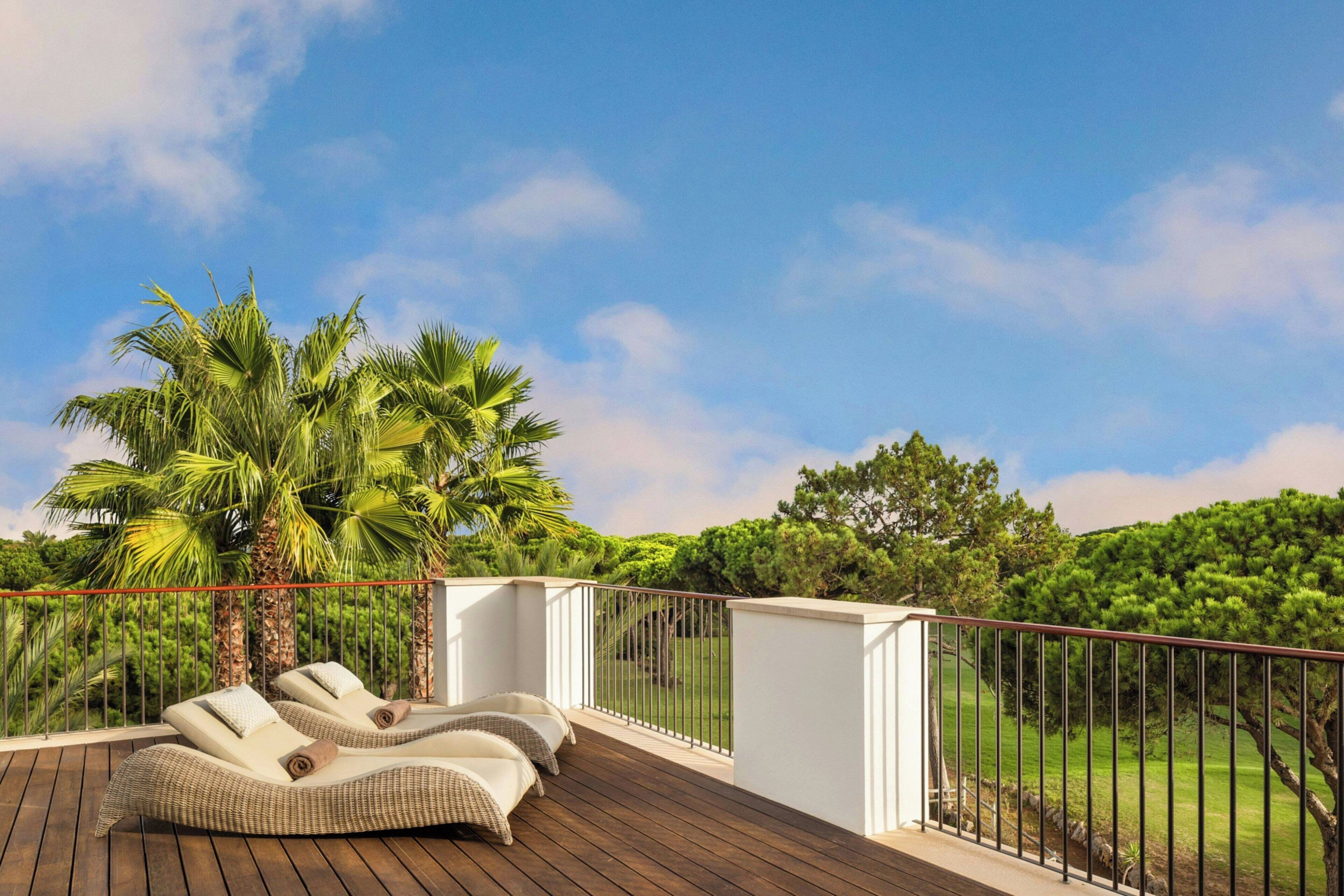 Una terraza de madera con dos sillones de descanso y una palmera.