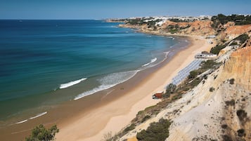 A coastal beach with a sandy shore, a few umbrellas, and a building on the cliff.