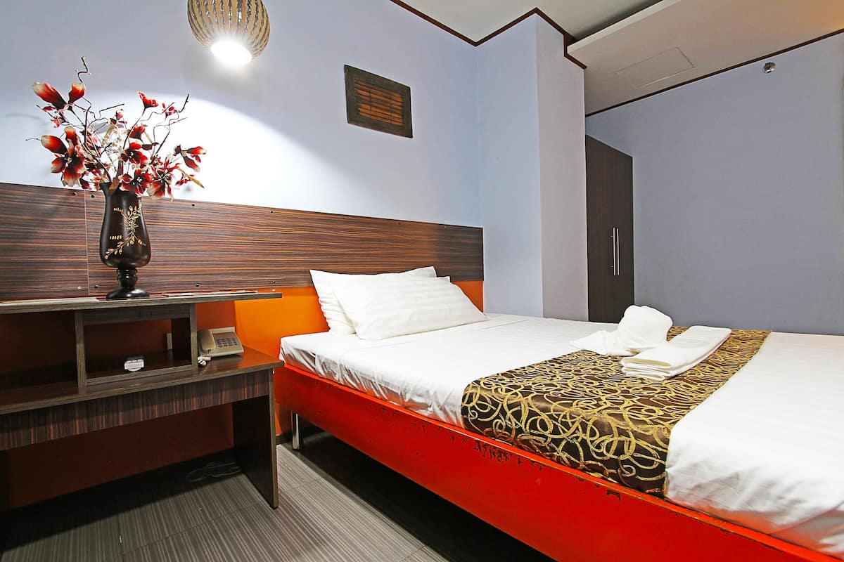 A hotel room with a bed, a nightstand, a vase with flowers, and a wooden headboard.
