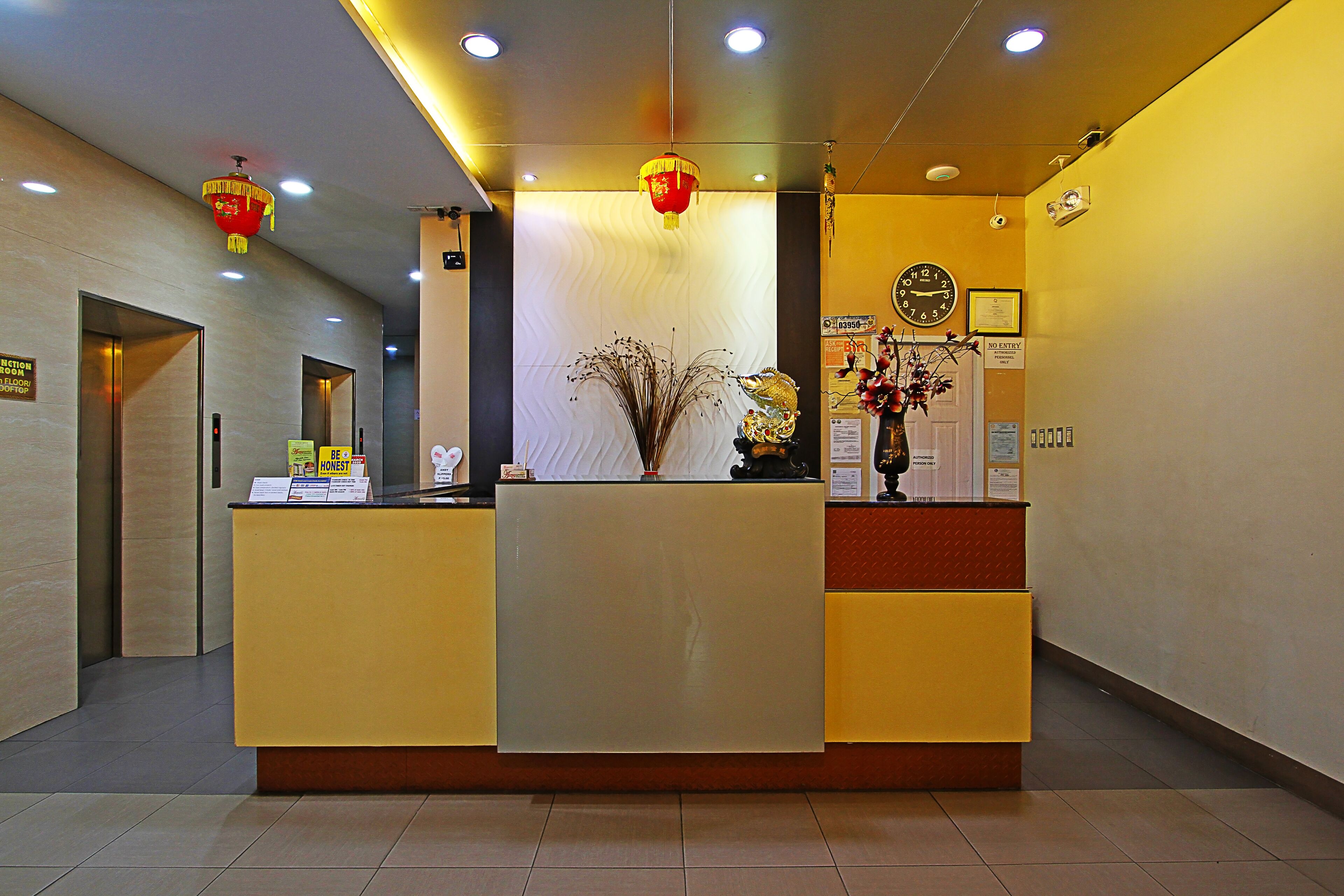A reception desk with a clock, a vase with dried plants, and a red lantern.