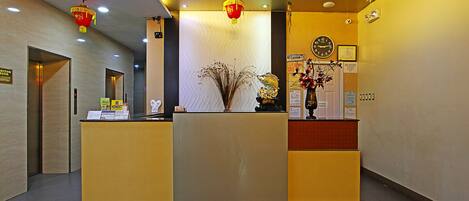 A reception desk with a clock, a vase with dried plants, and a red lantern.