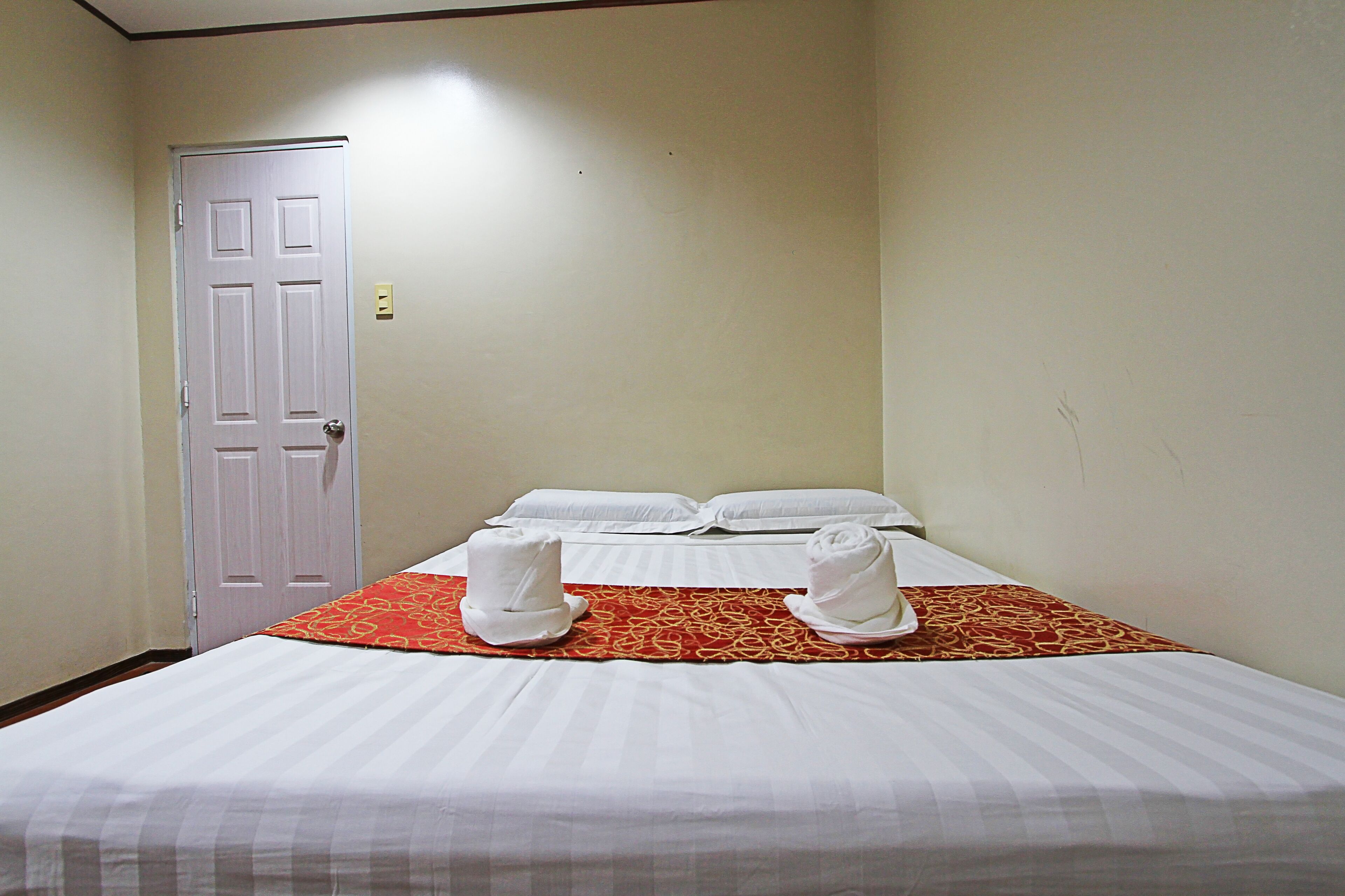 A hotel room with a bed, a door, and a red patterned bedspread.