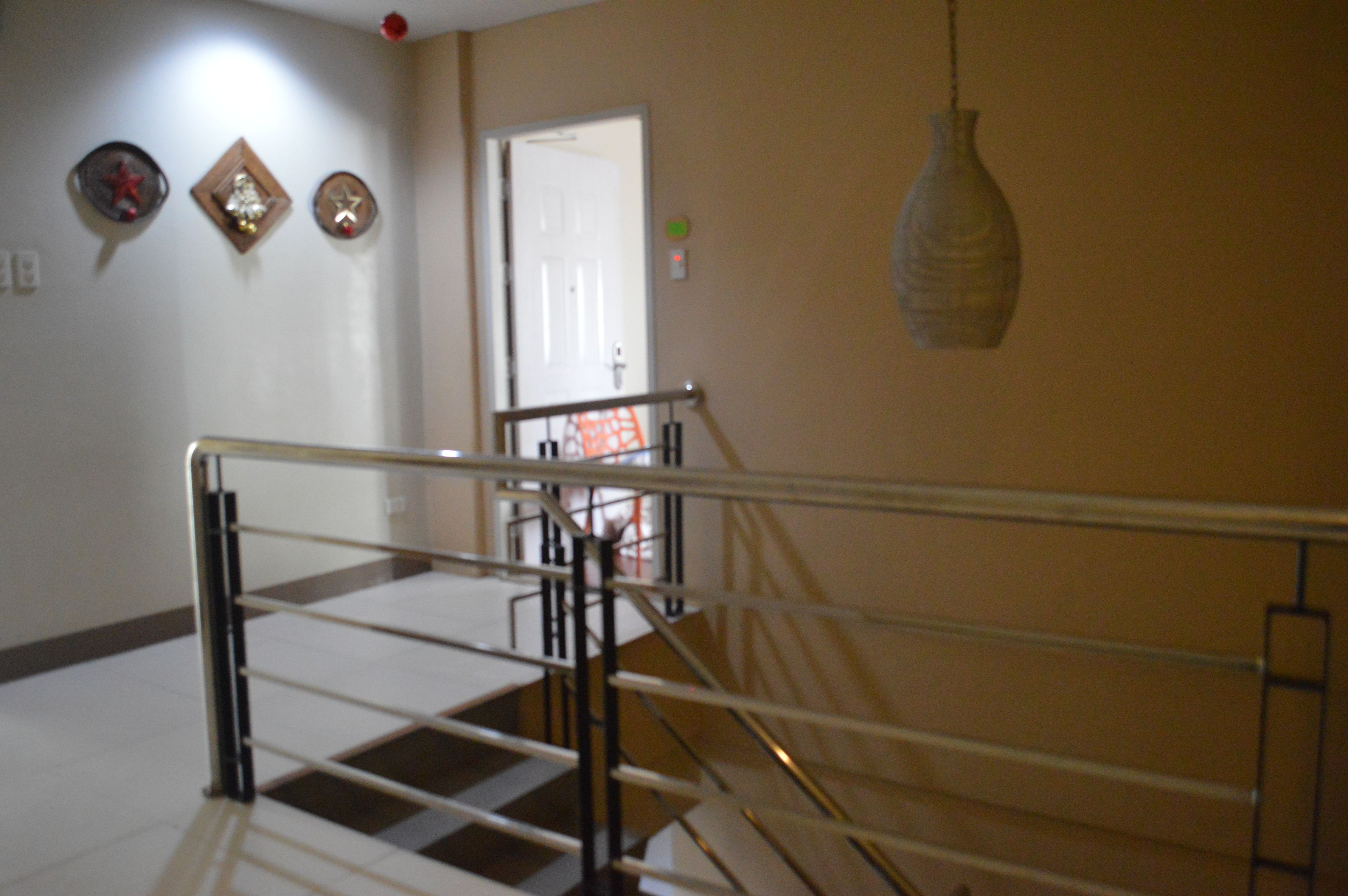 Una escalera con barandillas metálicas, una puerta en la parte superior y una lámpara colgante.