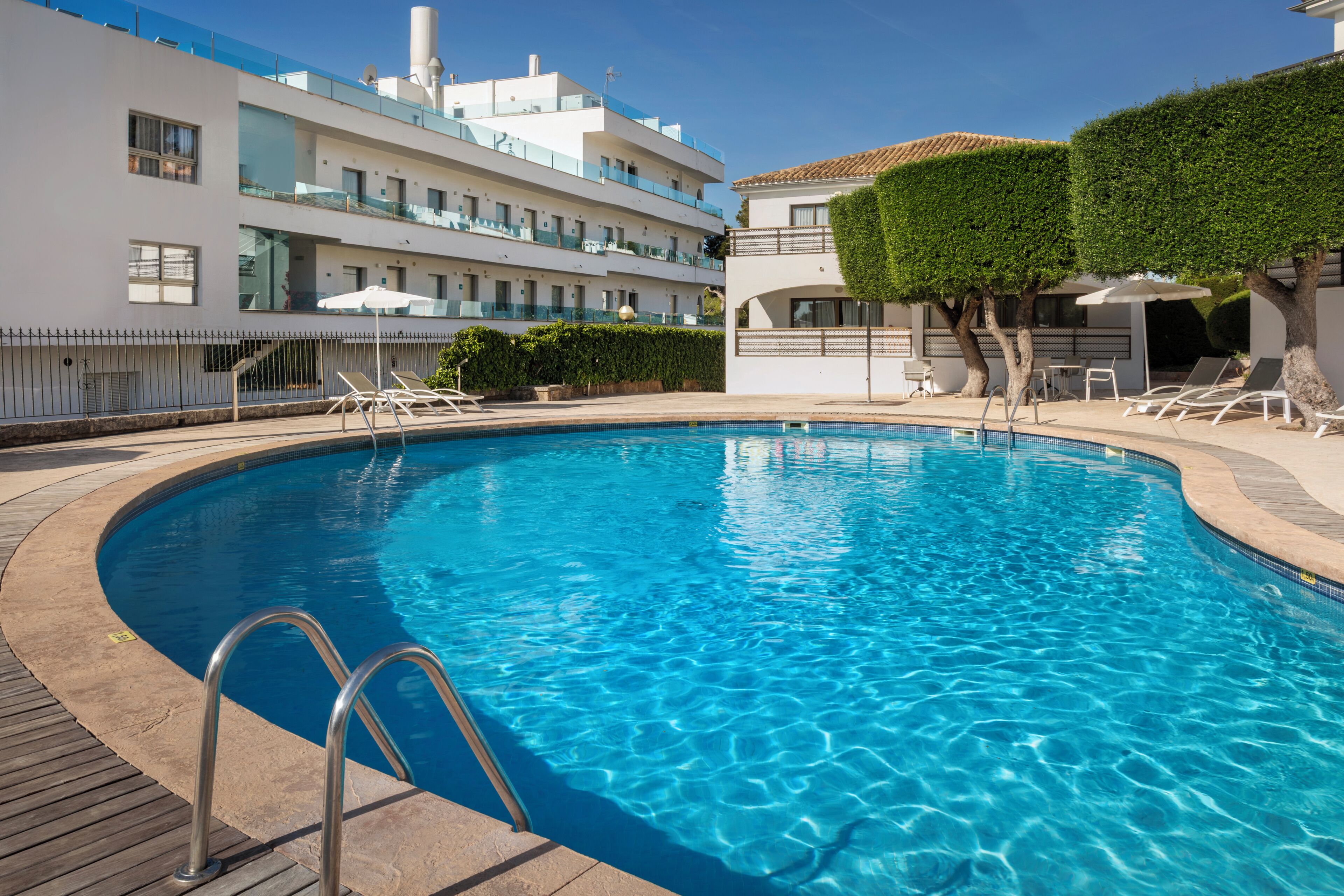 A swimming pool with a wooden deck, lounge chairs, and a modern building with balconies.