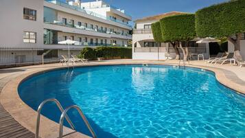 A swimming pool with a wooden deck, lounge chairs, and a modern building with balconies.