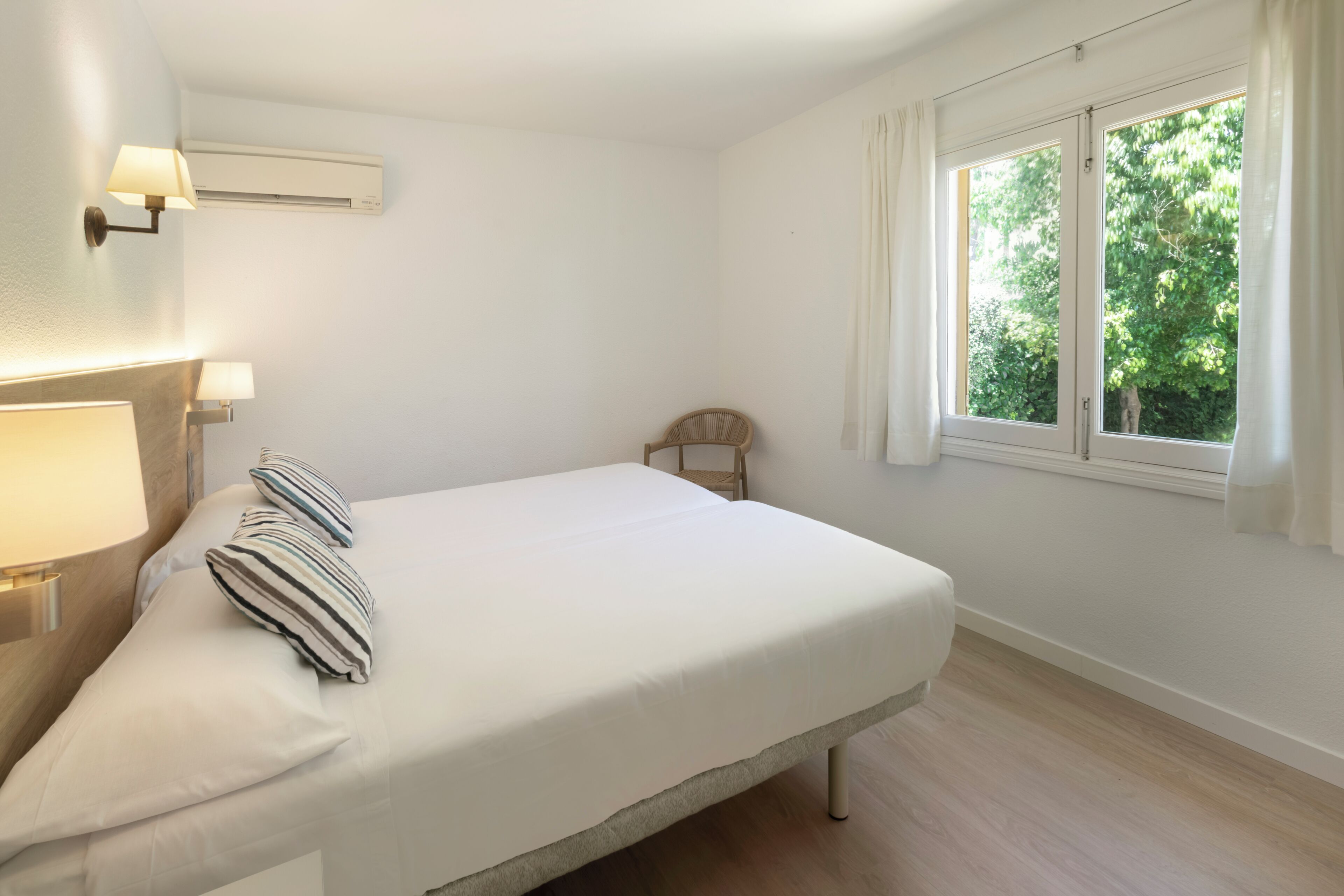 A bedroom with a bed, a chair, a window, and wall-mounted lights.