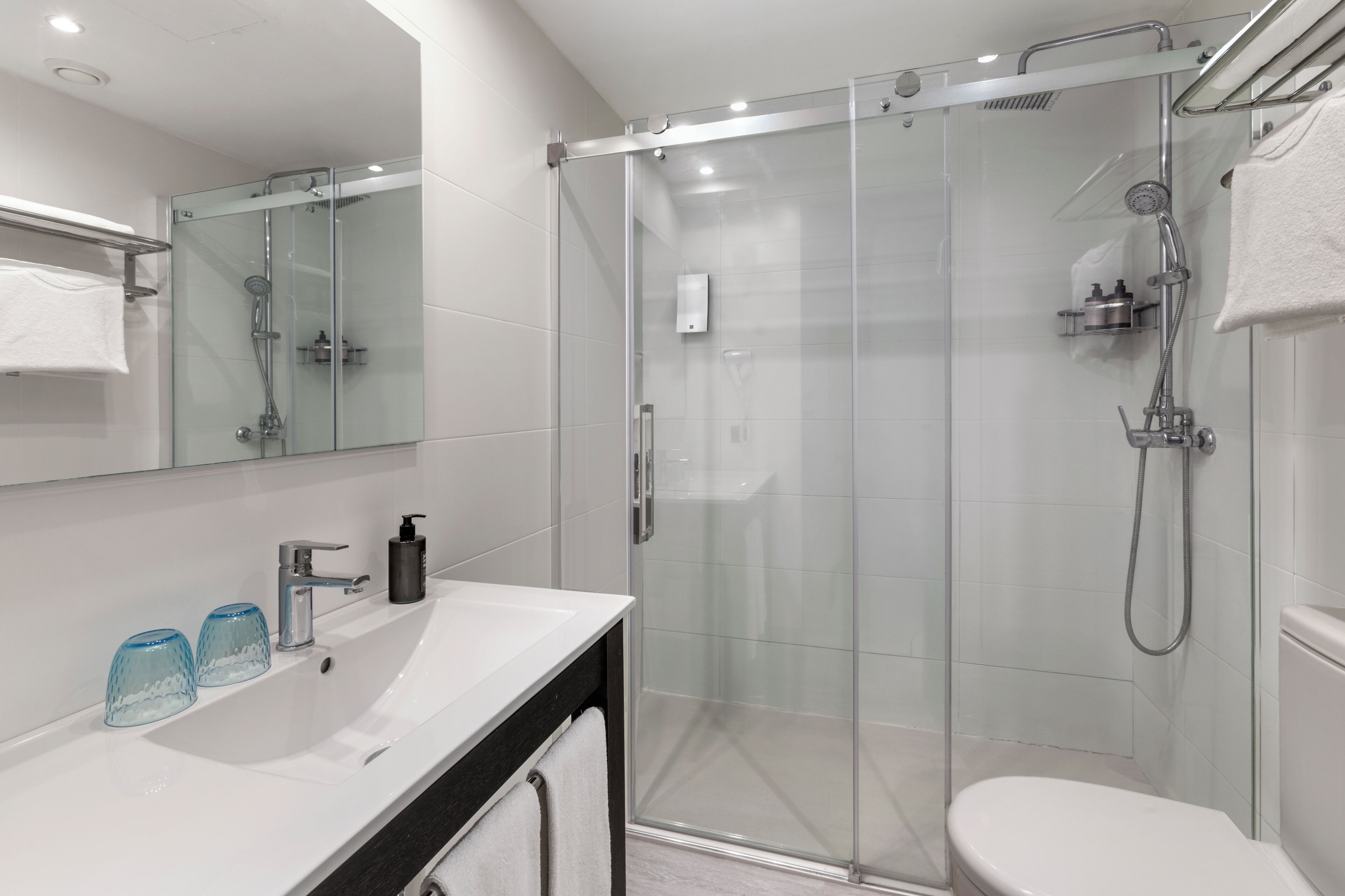 A modern bathroom with a glass-enclosed shower, a white sink with a black countertop, and a large mirror.