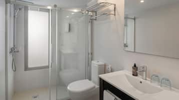 Un baño moderno con ducha de vidrio, inodoro blanco, lavamanos con espejo y un perchero para toallas.