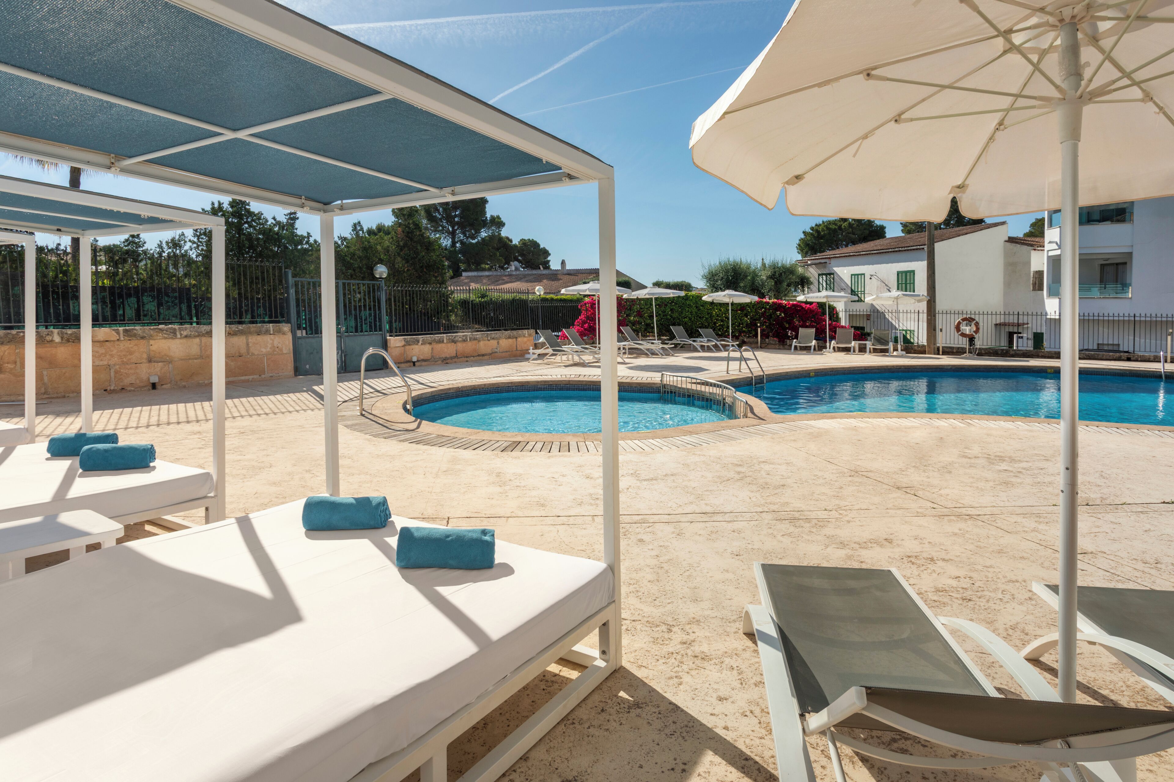 Un área junto a la piscina con sillas de descanso, sombrillas y un espacio de estar techado.