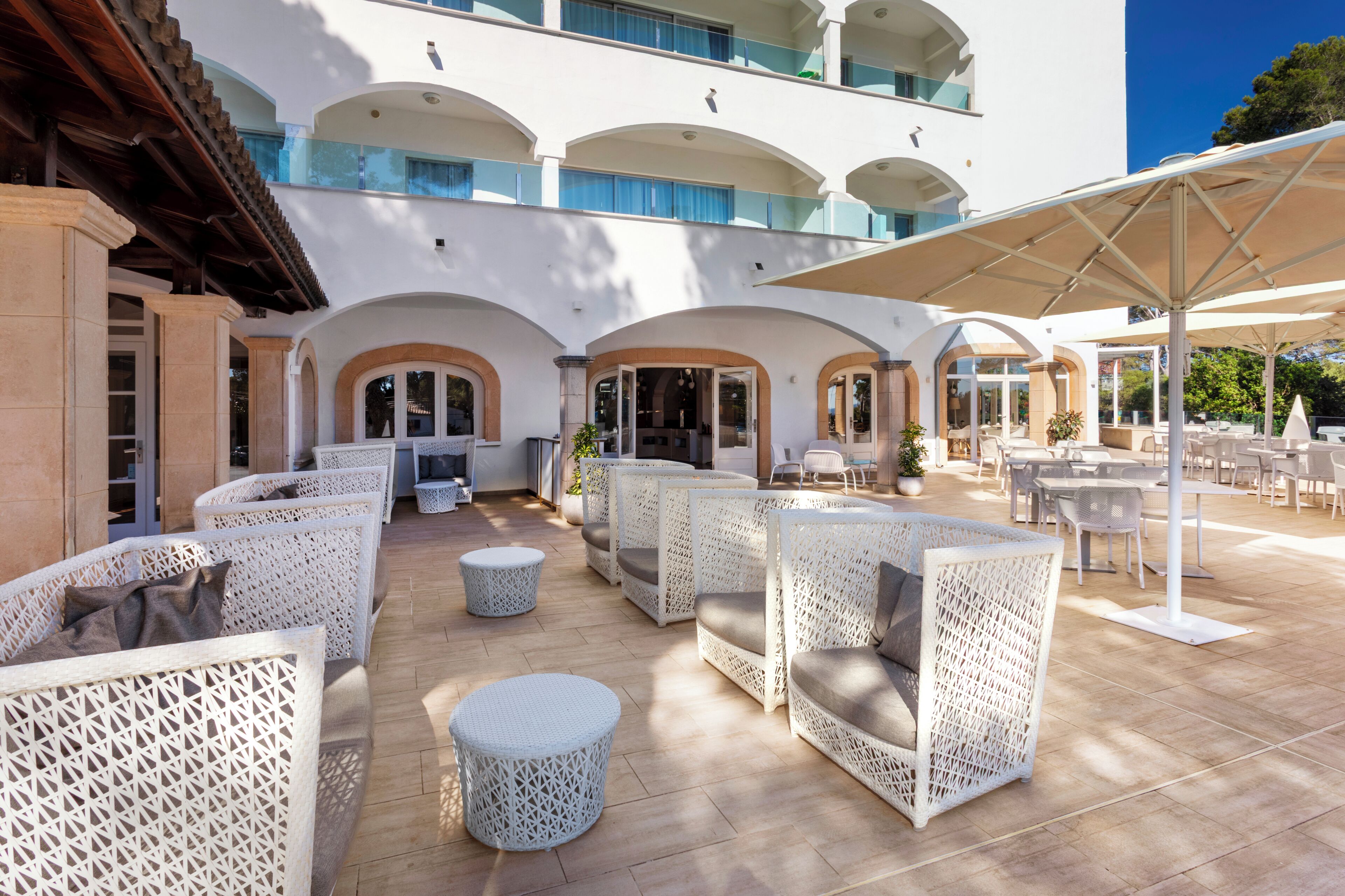 An outdoor seating area with wicker furniture, a covered patio, and a building with arched windows and balconies.