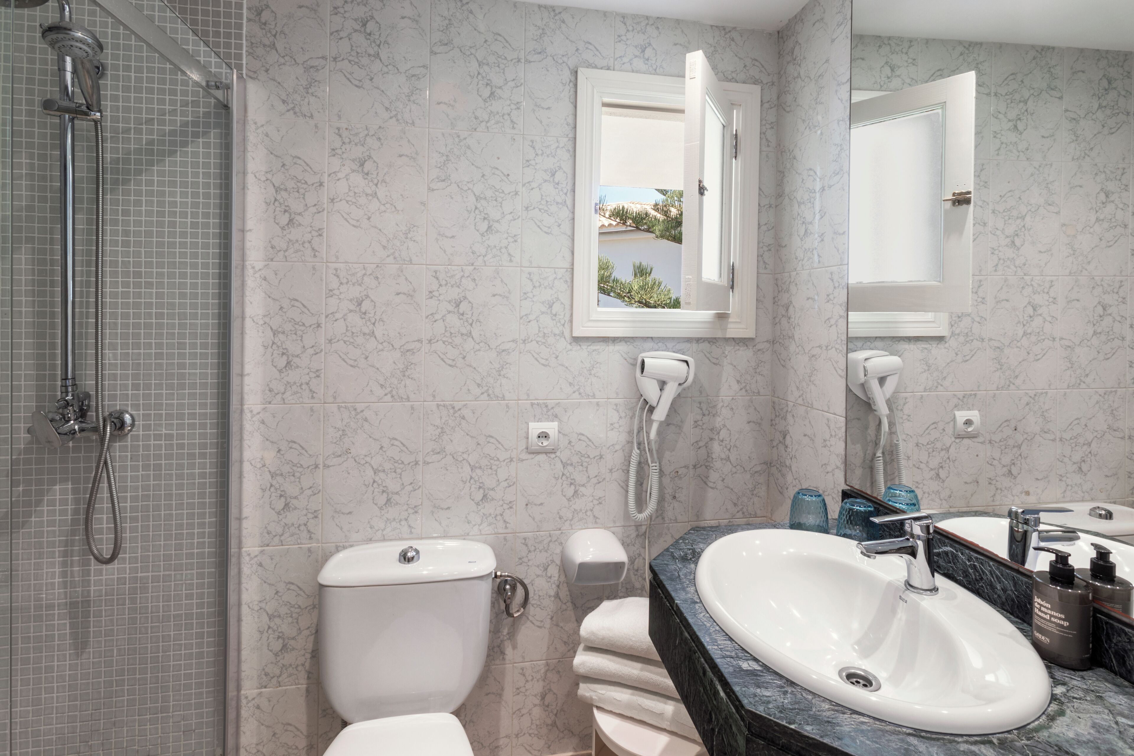 A bathroom with a shower, toilet, sink, and a window with a view.