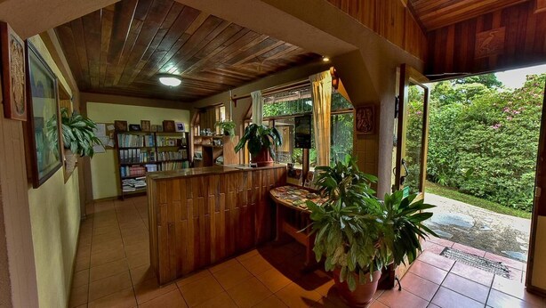 A wooden interior with a reception desk, bookshelves, and potted plants. - Hospedaje Mariposa (Monteverde)