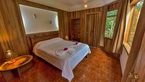 A wooden-paneled room with a bed, a nightstand, a window, and a wall-mounted TV. - Hospedaje Mariposa (Monteverde)
