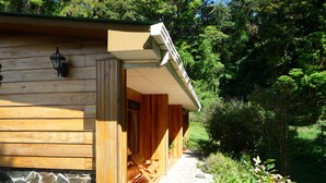A wooden cabin with a stone foundation, a covered porch, and a stone pathway leading to the entrance. - Hospedaje Mariposa (Monteverde)
