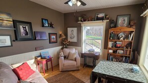 A cozy living room with a sofa, a chair, a small table, and a bookshelf. There is a window with a view of the outdoors.