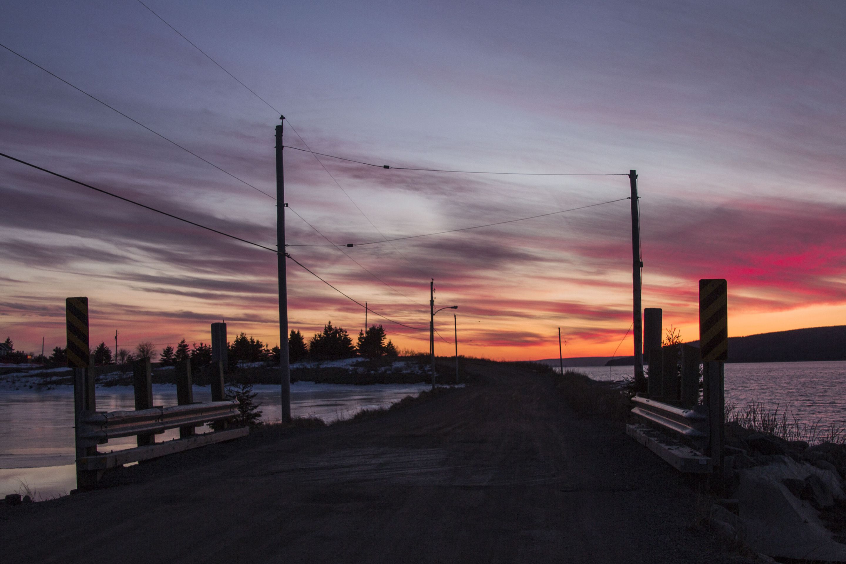 A rural road leading to a body of water with a sunset sky.
