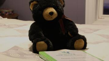 A black teddy bear sitting on a bed with a green folder labeled "Guest Information" beside it.