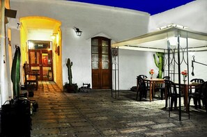 A courtyard with a wooden door, a covered seating area, and a narrow alleyway.