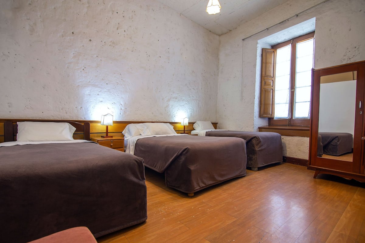 Una habitación con tres camas, piso de madera y un ventanal grande.