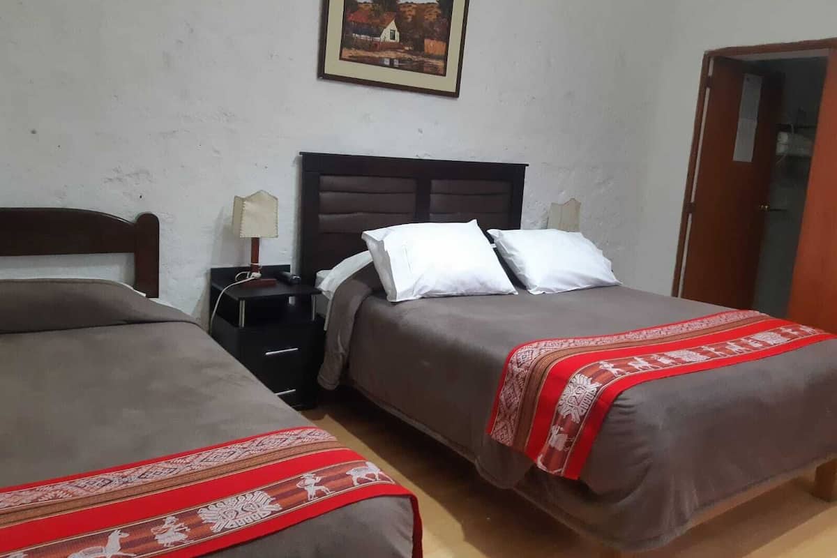 Una habitación con dos camas, una mesita de noche, una lámpara, un cuadro en la pared y una puerta.