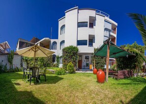 A multi-story building with a circular facade, outdoor seating with a table and chairs, and a small garden area.